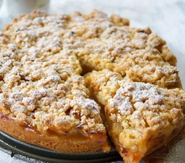 Omas Apfelkuchen mit Streusel auf einem Teller, serviert mit frischen Äpfeln.